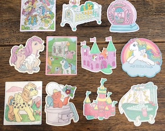 May include: A set of ten My Little Pony stickers featuring various scenes and characters. The stickers are colorful and feature pastel colors, including pink, blue, green, and yellow. The stickers depict a crib, a castle, a bathtub, a pony with a bottle of perfume, a pony with a brush, a pony with a bucket of soap, a pony with a crown, a pony with a flower, and a pony with a heart. The stickers are perfect for adding a touch of whimsy to any project.