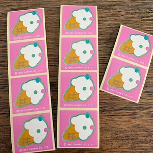 May include: A collection of vintage stickers featuring an ice cream cone design. Each sticker has a pink background with a white ice cream scoop, a yellow cone, and a blue cherry on top. The text "©1983 SANRIO CO. LTD." is printed on each sticker.