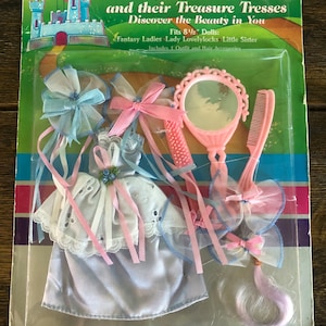 Könnte beinhalten: Eine Packung Fantasy Ladies Puppen-Accessoires mit einem blau-weißen Kleid, rosa-weißen Bändern, einem rosa Haarteil, einem rosa Kamm und einem rosa Handspiegel. Die Verpackung enthält den Text "Fantasy Ladies and their Treasure Tresses Discover the Beauty in You" und "Fits 8 1/2" Dolls: Fantasy Ladies Lady Lovelylocks Little Sister Includes 1 Outfit and Hair Accessories by  TOTSY".