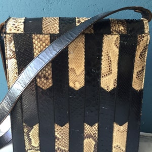 May include: A black and brown snakeskin shoulder bag with a long strap. The bag is made of multiple pieces of snakeskin sewn together in a striped pattern.