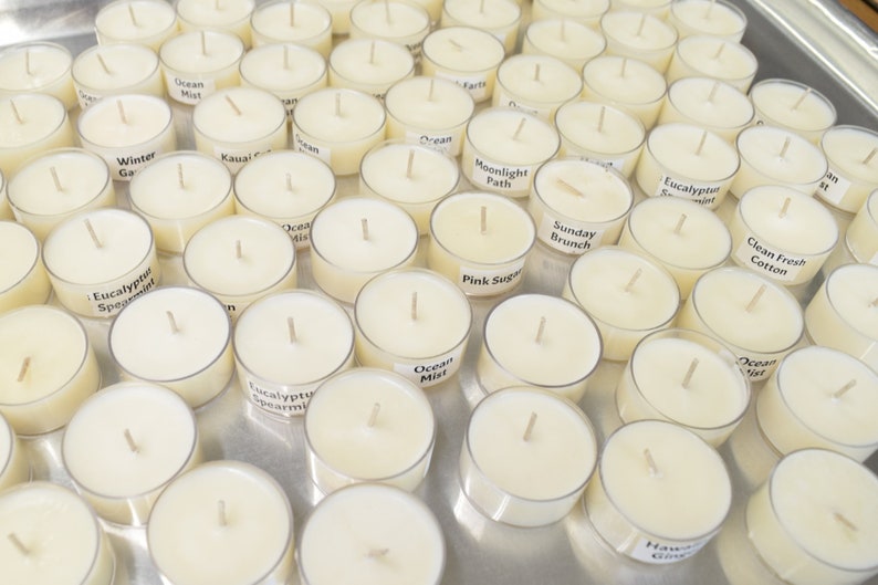 May include: A tray of white tea light candles with various scents, including Ocean Mist, Eucalyptus Spearmint, Winter Garden, Kauai, Moonlight Path, Pink Sugar, Sunday Brunch, Clean Fresh Cotton, and Hawaiian Ginger.