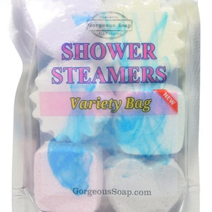 May include: A clear plastic bag filled with six colorful shower steamers in various shapes. The bag has a label that reads "Homemade Gorgeous Soap All Natural Shower Steamers Variety Bag New". The website address "GorgeousSoap.com" is printed on the bottom of the bag.