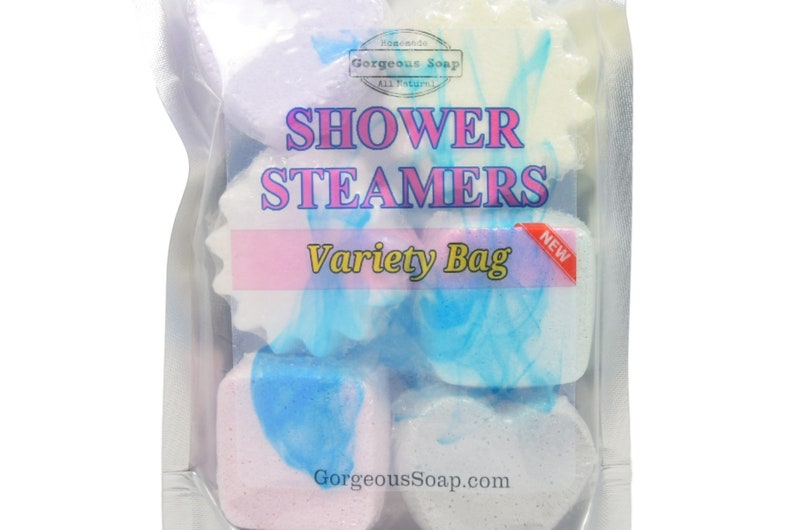 May include: A clear plastic bag filled with six colorful shower steamers in various shapes. The bag has a label that reads "Homemade Gorgeous Soap All Natural Shower Steamers Variety Bag New". The website address "GorgeousSoap.com" is printed on the bottom of the bag.