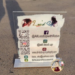 May include: A white acrylic sign with a glitter background and a QR code. The sign has the text "All Loc'd Up!" and social media handles: @AllLocdUpwithRobin, @all.locd.up, www.all-locd-up.myshopify.com, locs_alu@yahoo.com, and $RobinRouse44.