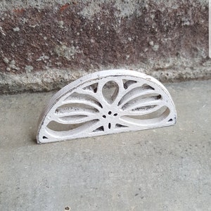 以下が含まれることがあります： 花のようなカットアウトデザインが施された、白く塗られた木製の半円形の装飾品