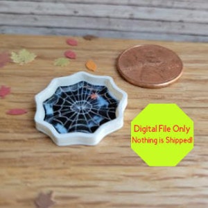 Könnte beinhalten: Ein weißes Plastiktablett in Form eines Spinnennetzes mit einem schwarzen Spinnennetz-Design und einer kleinen orangefarbenen Spinne in der Mitte. Das Tablett ist etwa so groß wie eine deutsche Ein-Cent-Münze.