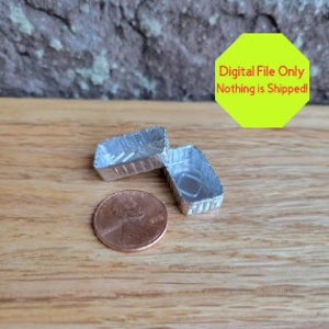 May include: Two small, silver, foil food containers, one open and one closed, next to a US penny.