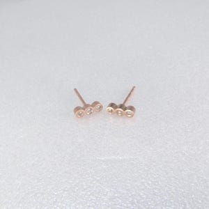 Gli orecchini a perno con tre pietre sono disponibili in oro rosa, oro giallo o argento sterling e sono incastonati con topazio blu Londra o diamanti bianchi.