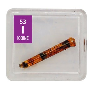 May include: A clear plastic display case with a purple label that reads "53 I IODINE". Inside the case is a brown, crystalline sample of iodine.