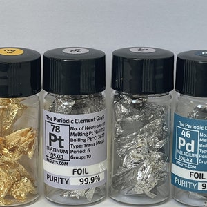 May include: Six small glass vials containing foil samples of the elements gold, platinum, palladium, and silver. Each vial has a label with the element's symbol, atomic number, name, and purity. The labels also include information about the element's melting point, boiling point, and group on the periodic table.