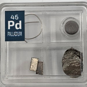 Puede incluir: Un recipiente de plástico transparente con cuatro compartimentos. El compartimento superior tiene una etiqueta azul con el texto "46 Pd Palladium". Los otros compartimentos contienen un pequeño trozo de metal, una bobina de alambre, un pequeño disco gris y un trozo de metal más grande.