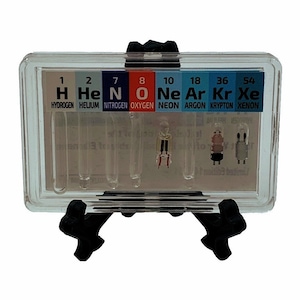 Puede incluir: Una vitrina de plástico transparente con un soporte negro, que contiene pequeños tubos de vidrio llenos de gases nobles: hidrógeno, helio, nitrógeno, oxígeno, neón, argón, kriptón y xenón. Cada tubo está etiquetado con el símbolo, el número atómico y el nombre del elemento.