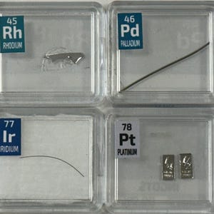 May include: A collection of small, clear plastic containers, each containing a sample of a different element. The elements are labeled with their atomic number and symbol, and their names are listed below. The elements included are Ruthenium, Rhodium, Palladium, Silver, Osmium, Iridium, Platinum, and Gold.