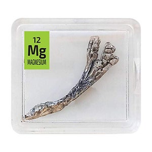 May include: A silver magnesium metal sample in a clear plastic case. The case has a green label with the element symbol "Mg" and the word "MAGNESIUM". The sample is shaped like a claw.