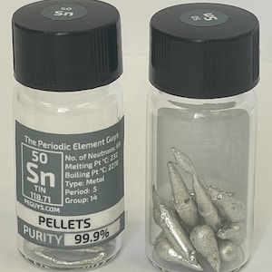 May include: Two clear glass vials with black lids containing small silver tin pellets. The label on the vial on the left reads "The Periodic Element Guys", "50 Sn", "TIN", "118.71", "PEGUYS.COM", "PELLETS", "PURITY 99.9%".
