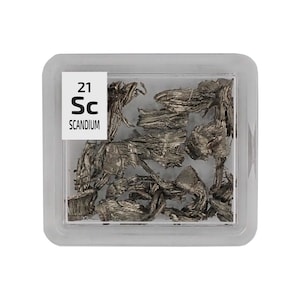 以下が含まれることがあります： 白いラベルに「21 Sc SCANDIUM」と書かれた小さな透明なプラスチック容器。容器の中には、銀灰色の小さな金属片が入っています。