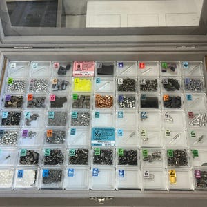 Puede incluir: Una colección de elementos en una caja de plástico transparente con etiquetas para cada elemento. Los elementos están dispuestos en filas y columnas, y cada elemento está en un pequeño compartimento. La caja está cerrada y tiene un forro de terciopelo gris.