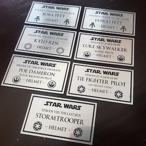 May include: A set of ten silver metal Star Wars character nameplates. Each nameplate features a character's name, episode number, and helmet icon. The nameplates include Boba Fett, Kylo Ren, Jango Fett, Luke Skywalker, Poe Dameron, Tie Fighter Pilot, and Stormtrooper.