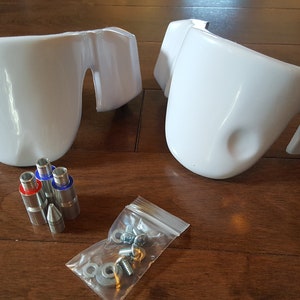 May include: Two white plastic parts with a set of screws and metal pins. The parts are designed to be attached to a larger object.