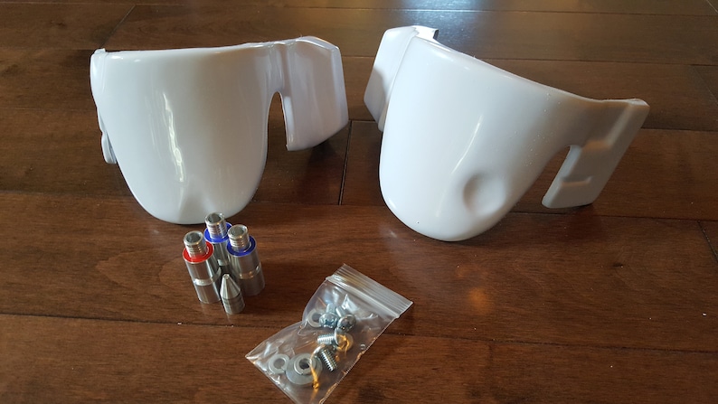 May include: Two white plastic parts with a set of screws and metal pins. The parts are designed to be attached to a larger object.