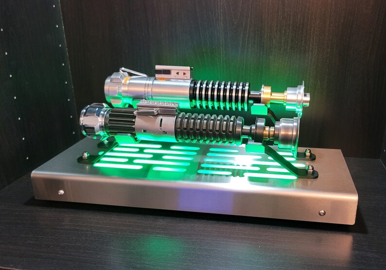 May include: Two silver and black lightsabers with green lights on a silver metal stand with a green light grid.