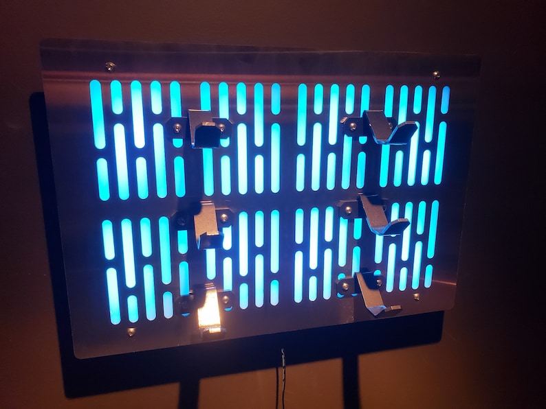 May include: A metal wall art piece with a blue light behind it. The art piece is shaped like a grid with a pattern of lines and holes. There are several metal pieces attached to the front of the art piece.