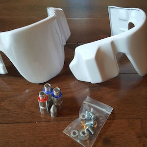 May include: Two white plastic pieces with a set of screws and washers in a plastic bag. The pieces have a curved shape and are likely parts for a model or toy.