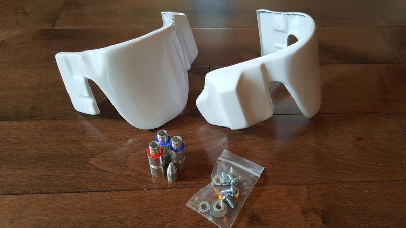 May include: Two white plastic pieces with a set of screws and washers in a plastic bag. The pieces have a curved shape and are likely parts for a model or toy.