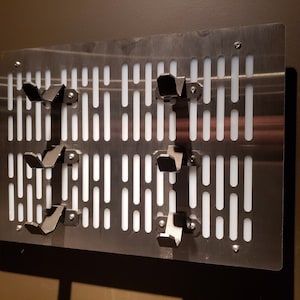 May include: A metal wall panel with a grid pattern and several black metal hooks. The panel has a white background and is designed to resemble the Death Star from the Star Wars franchise.