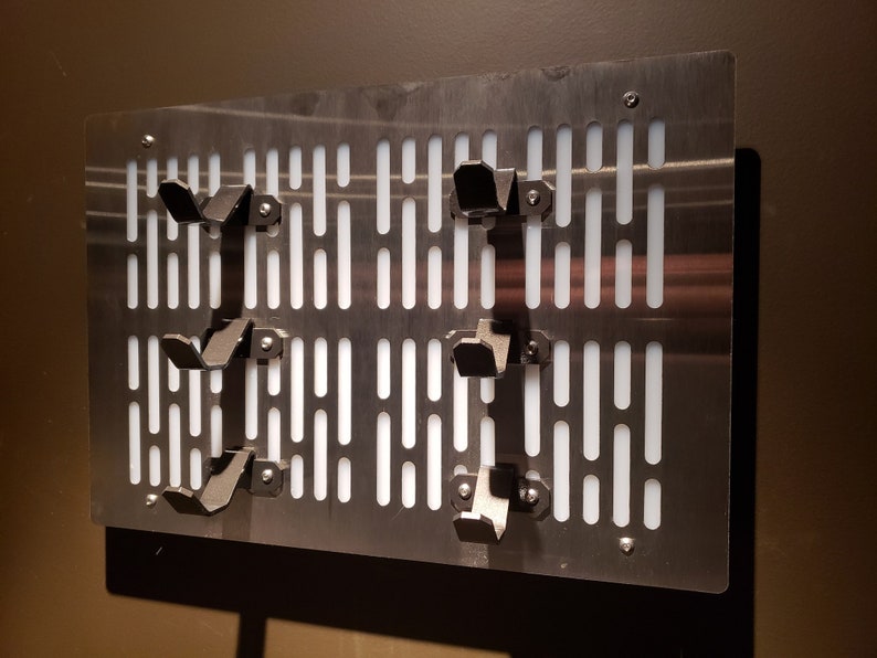 May include: A metal wall panel with a grid pattern and several black metal hooks. The panel has a white background and is designed to resemble the Death Star from the Star Wars franchise.