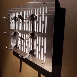 May include: A silver metal wall-mounted rack with multiple hooks for hanging items. The rack has a grid pattern with white rectangular openings.