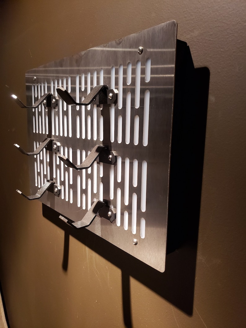 May include: A silver metal wall-mounted rack with multiple hooks for hanging items. The rack has a grid pattern with white rectangular openings.