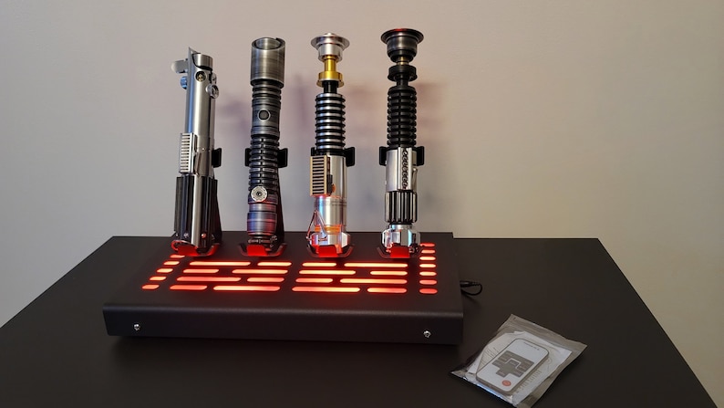 Pode incluir: Quatro r&eacute;plicas de sabres de luz em um suporte preto com luzes LED vermelhas. Os sabres de luz s&atilde;o prateados, pretos, dourados e uma combina&ccedil;&atilde;o de prata e preto.