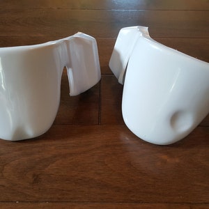 May include: Two white plastic pieces, possibly for a costume or prop. They are shaped like curved, rounded pieces with a flat edge on one side.