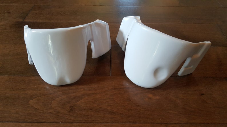 May include: Two white plastic pieces, possibly for a costume or prop. They are shaped like curved, rounded pieces with a flat edge on one side.