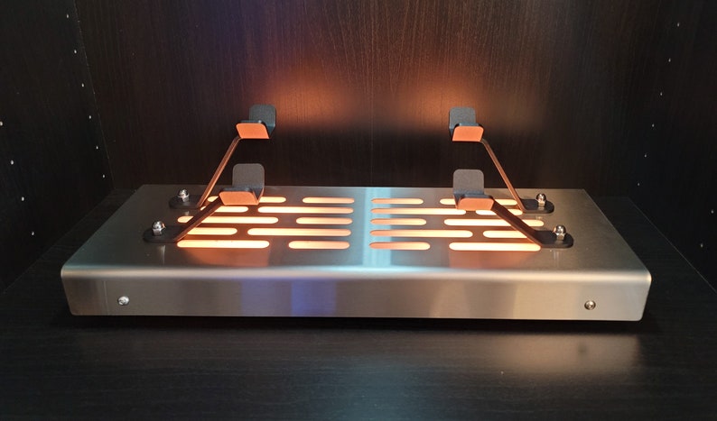 May include: A silver metal platform with a grid pattern and two black metal arms with copper-colored accents. The platform is illuminated from below, creating a warm glow.