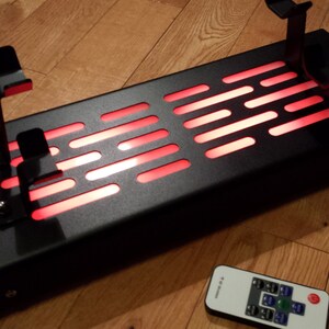 May include: A black metal stand with a red light-up panel and two metal hooks. The stand is controlled by a remote control with buttons.