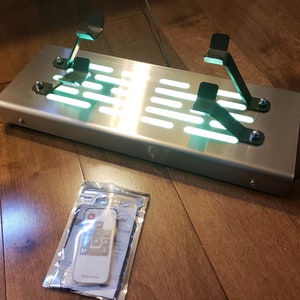 May include: A brushed stainless steel pedal platform with two black metal pedal mounts. The platform has a green LED light strip running along the bottom. A remote control is included in a clear plastic bag.