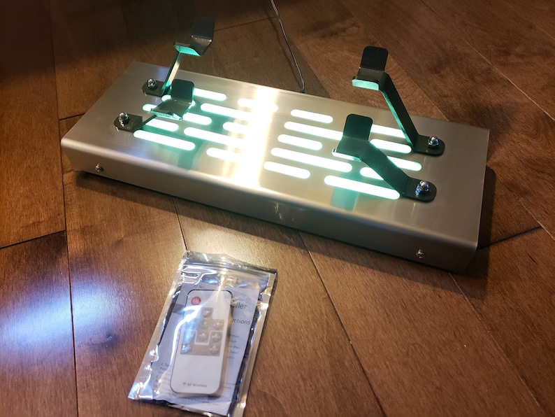 May include: A brushed stainless steel pedal platform with two black metal pedal mounts. The platform has a green LED light strip running along the bottom. A remote control is included in a clear plastic bag.