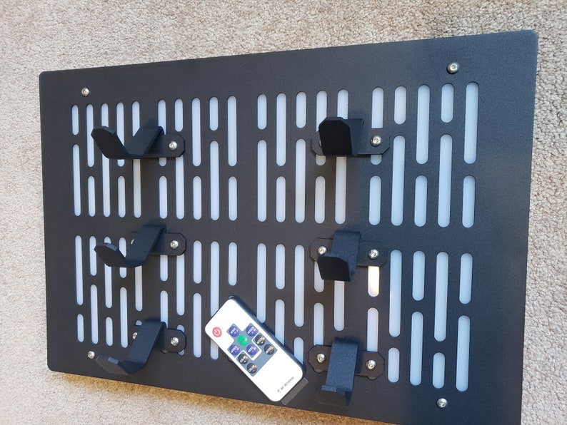 May include: A black metal wall organizer with a white grid pattern and multiple hooks. The organizer has a Star Wars inspired design. A remote control is sitting on the organizer.