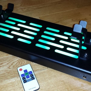 May include: A black metal Star Wars themed light-up display with a green light and two control panels. The display is controlled by a remote control with a green button.