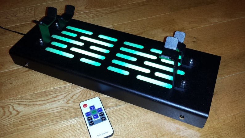 May include: A black metal Star Wars themed light-up display with a green light and two control panels. The display is controlled by a remote control with a green button.