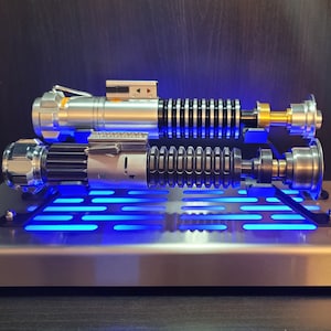 May include: Two silver and black lightsabers with blue lights on a silver stand with a grid pattern.