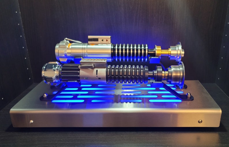 May include: Two silver and black lightsabers with blue lights on a silver stand with a grid pattern.