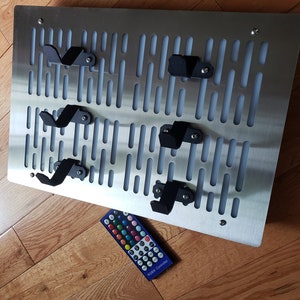 May include: A silver metal wall mounted pegboard with black hooks and a remote control labeled "RGB Controller".