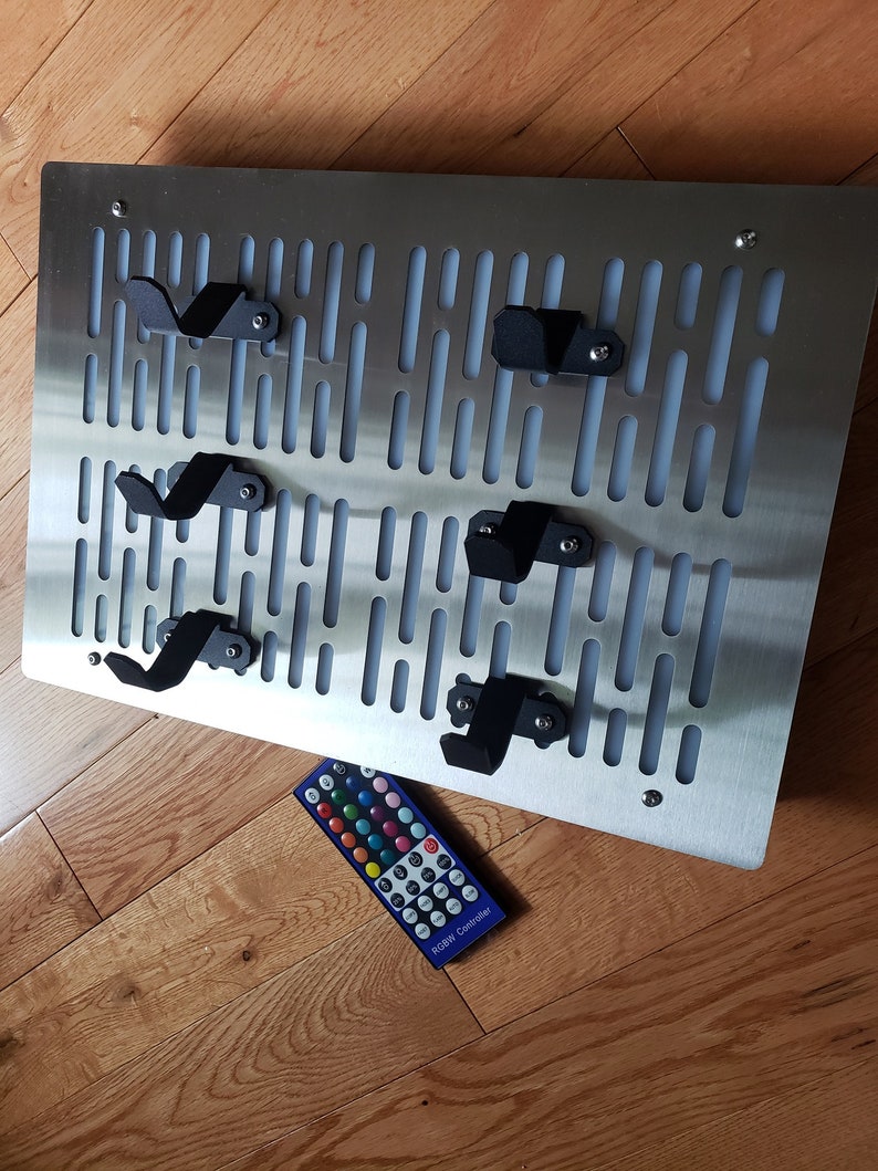 May include: A silver metal wall mounted pegboard with black hooks and a remote control labeled "RGB Controller".