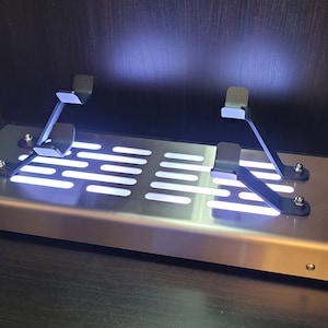 May include: A silver metal platform with a grid pattern and two black metal brackets. The platform is illuminated with white LED lights.