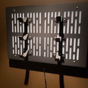 May include: A black metal wall-mounted storage rack with a white grid pattern and multiple hooks. The rack has a cord hanging from the bottom.