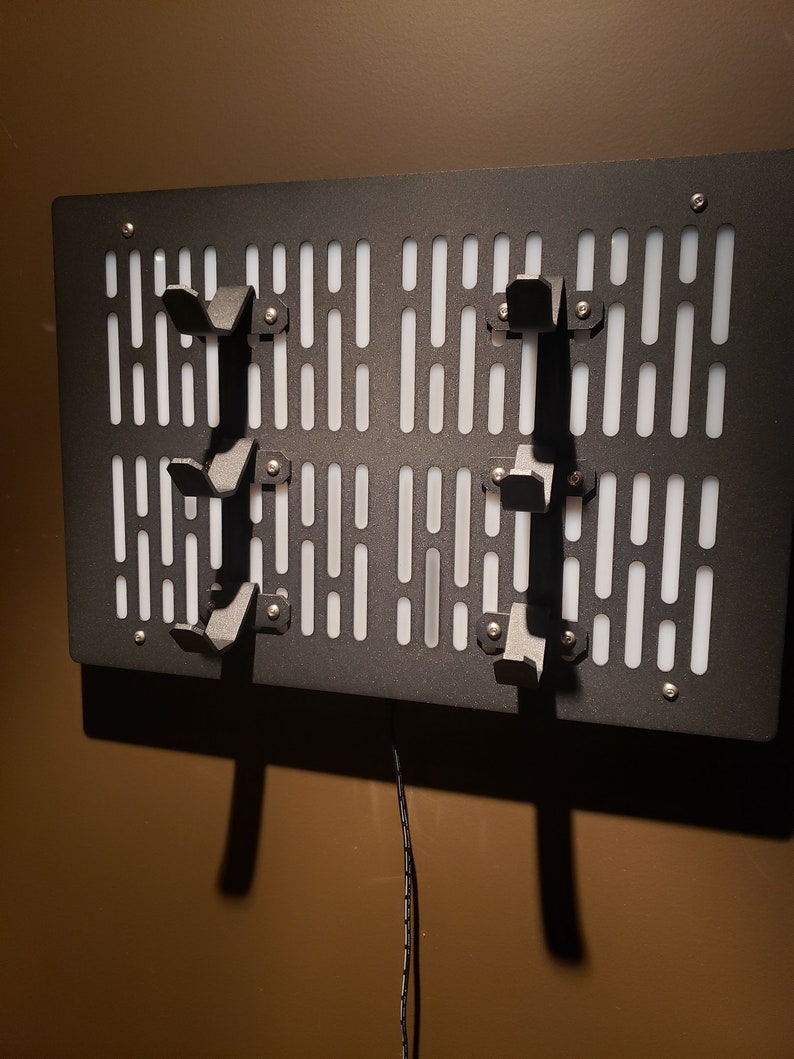 May include: A black metal wall-mounted storage rack with a white grid pattern and multiple hooks. The rack has a cord hanging from the bottom.