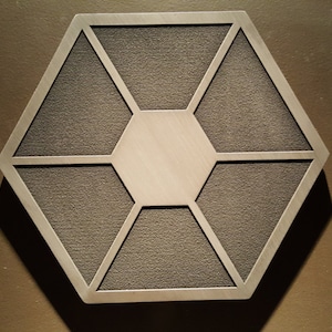 May include: A silver-coloured, hexagonal-shaped metal wall decor with a textured surface. The decor has a central hexagon shape with six smaller hexagons surrounding it.